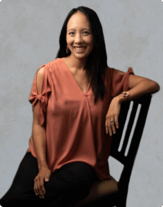 A young therapist is sitting on a chair wearing black trousers and a light brown skirt.