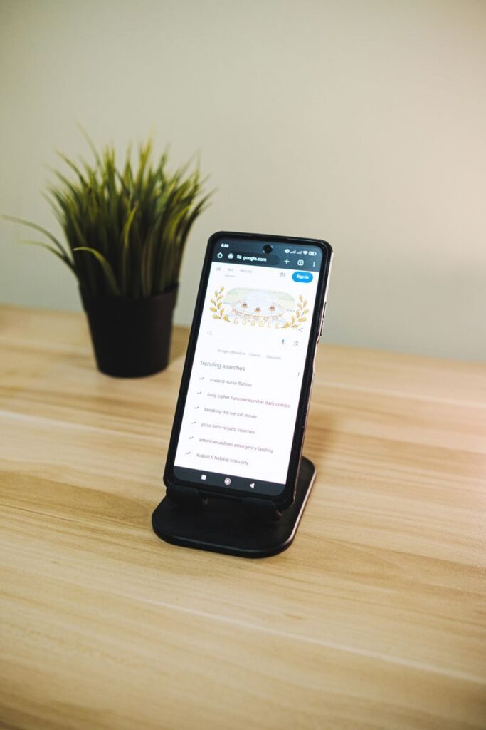 A sleek smartphone on a wooden desk next to a green potted plant, showcasing a technology theme.